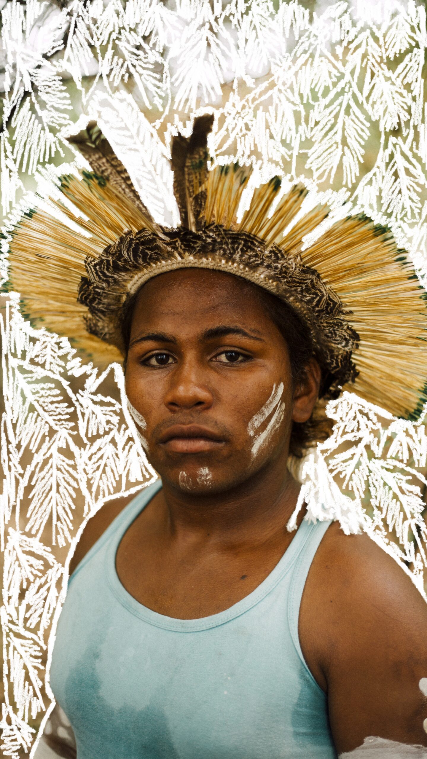 Portrait from the 'Origem' series, featuring illustrative background added through AR technology. A person wearing a blue vest with a headdress made of natural materials. They have two white stripes of paint across each cheek and on the chin. The background of the portrait is covered in white illustrated leaves which are digitally created.