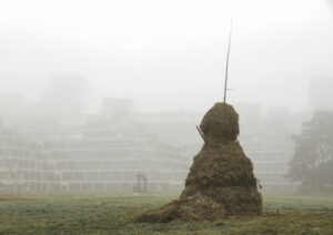 A little boy standing beside a Sculpture made from a stack of hay and timber.