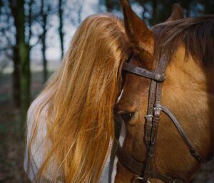 A red haired woman with a brown horse in a woodland