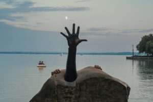 A sculpture depicting an arm reaching upwards, and behind it two hands appearing to climb onto the sculpture itself.